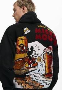 Felpa nera con design a maglia che presenta colorati personaggi Disney, botti e motivi di birra sul retro.