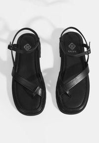Zwarte leren sandalen met een platte zool, voorzien van kruisbanden en een enkelband. Merken zijn in de binnenzool gedrukt.