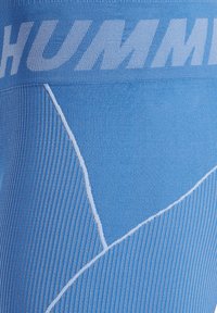 Ljusblå träningstights med ribbad textur, med en vit logotyp vid midjan och kontrasterande sömdetaljer i ett geometriskt mönster.