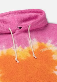 Fleece hoodie met een verloop van roze naar oranje, met een gestructureerde oppervlakte, witte trekkoorden en "TOMORROWLAND" gedrukt in het wit.