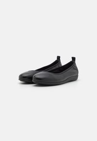 Une paire de ballerines en cuir noir avec des orteils ronds et des languettes, présentée sur un fond blanc uni.