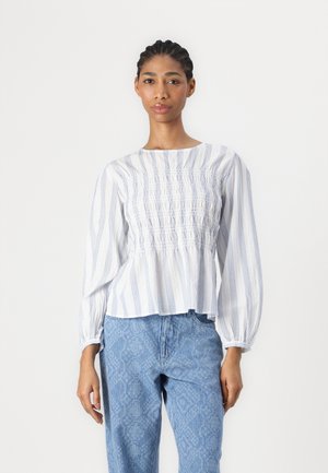 Hvit bluse med blå vertikale striper, smocket liv, og lange puffermer, kombinert med lyseblå mønstrede jeans.
