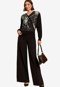 Svart tröja med flerfärgad abstrakt tryck på framsidan, kombinerad med vida svarta byxor. Inkluderar en svart handväska och högklackade skor.