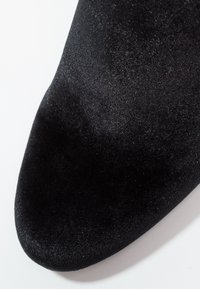 Bout de chaussure en velours noir doux avec une forme arrondie sur fond blanc.