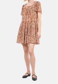 Vestido de estampado floral en crema claro, con escote cuadrado, mangas cortas abullonadas y falda en capas. Combinado con zapatos negros con tachuelas.
