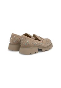 Beige suède loafers met dikke zolen, voorzien van een scala aan zilveren en lichtblauwe studs, die een robuust maar decoratief ontwerp tonen.