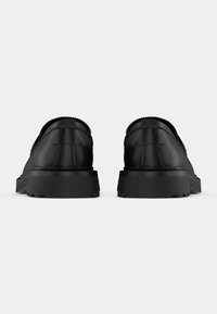 Black shoes with a smooth leather upper, rounded toe, and textured accents. Thick rubber soles with deep tread for grip. Overall minimalist design.