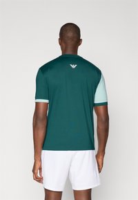 Camiseta atlética verde de manga corta con acentos de verde menta en las mangas, que presenta un logo en la parte superior de la espalda. Tela suave y ligera.