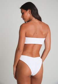 Ensemble de bikini blanc texturé comprenant un haut sans bretelles et un bas à grande taille, mettant en avant un design lisse et ajusté.
