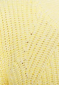 Ljusgul stickad tyg med ett texturerat mönster, som innehåller löpande stygn och en mjuk, något fluffig utseende.