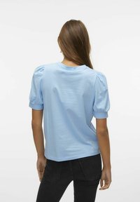 T-shirt de manga curta azul claro com mangas bufantes, decote redondo e um ajuste descontraído. O material parece suave, com uma textura lisa.