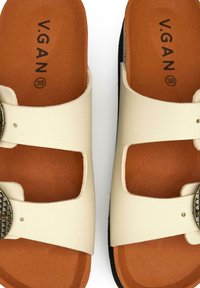 White vegan slides with two wide straps, decorative studded buckle, tan footbed, and black sole, size 38, featuring a smooth texture.