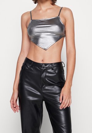 Frau trägt ein metallisch silbernes, bauchfreies Trägertop mit dünnen Trägern und schwarze hoch taillierte Kunstlederhose.