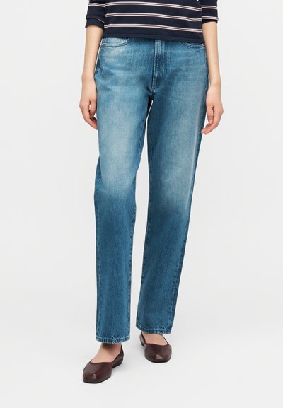 Jean droit bleu clair en denim, avec finition délavée et design classique à cinq poches, associé à des ballerines marron.