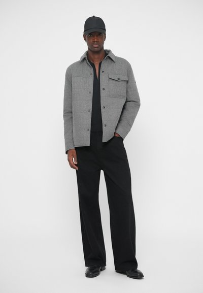 Harmaa villasekoite takki, jossa on kauluskäänteet, rintatasku ja etunapit, yhdistettynä mustiin leveälahkeisiin housuihin ja mustaan luodinhoitoon.