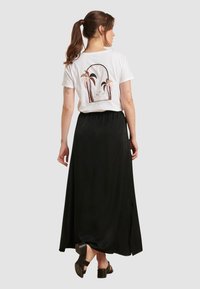 Witte t-shirt met palmboomgrafiek in pastel kleuren, gecombineerd met een lange zwarte rok met een zijsplit en chunky zwarte sandalen.