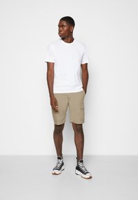 T-shirt blanc à col rond associé à un short cargo beige et des baskets montantes noires. Le short possède des poches latérales et une coupe décontractée.