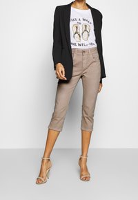 Blazer negro sobre una camiseta gráfica blanca con un diseño de chanclas, combinado con pantalones cortos beige y tacones nude con tira en el tobillo.