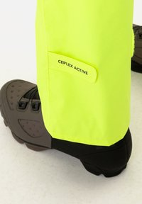 Yellow waterproof pant leg with textured surface, featuring a visible "CEPLEX ACTIVE" tag. Dark footwear with a rugged sole is partially shown.