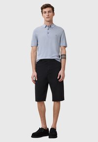 Ljusblå polo med korta ärmar, tre knappar och en liten logotyp; matchad med svarta knälånga shorts och svarta skor.