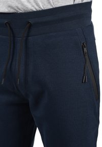 Navy blue joggers made of soft, textured fabric with a ribbed waistband, drawstring closure, and zippered pockets on the sides.
