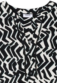 Kurzärmlige Bluse mit einem schwarz-weißen abstrakten Zickzackmuster, akzentuiert mit hellblauen Details und einem V-Ausschnitt. Das Material scheint weich zu sein.