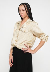 Béžová košeľa na zapínanie s geometrickým vzorom, s golierom, dvoma náprsními vreckami a vyhrnutými rukávmi; hodvábna textúra, ležérny strih.