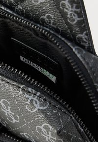 Mustast lukuga rahakott koos reljeefse logomustriga, tekstureeritud sünteetilise välisküljega ja kangaga vooderdatud siseosaga, kus on nähtav brändi silt.