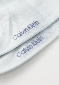 Meias de um azul claro dobradas, cada uma com "Calvin Klein" bordado em fio azul escuro perto da borda.