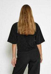 Juodas tekstūruotas viršus su trumpomis rankovėmis, turintis bangą primenančią tekstūrą. Suderintas su juodomis kelnėmis, pasižyminčiomis laisvu kirpimu ir lygiu audiniu.