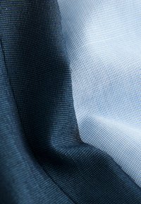 Gros plan sur un tissu étroitement tissé avec une section bleu foncé à côté d'une section bleu clair, montrant les détails de texture et de tissage.