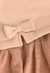 Ljusrosa plagg med en texturerad stickad överdel, som har en liten rosett detalj i midjan och en plisserad mesh-underdel.