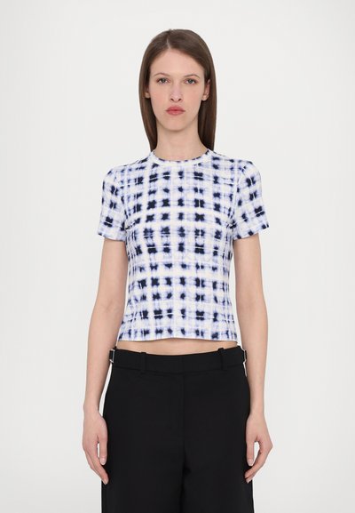 Rövid ujjú crop top fehér és tengerészkék batikolt mintával. Sima anyagból készült, kerek nyakkivágással és testhez simuló fazonnal. Fekete nadrággal párosítva.