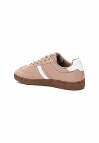 Zapatilla de deporte rosa claro hecha de material sintético, con una franja blanca de acento y suela de goma marrón. Punta redondeada y diseño con cordones.