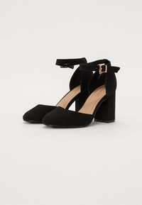 Svarta mocka högklackade skor med fyrkantig tå och blockklack. Vristrem med metallspänne. Sulan har en slät finish.