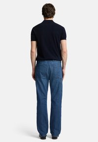 Polo shirt navy abbinato a pantaloni cargo in denim blu con più tasche posteriori e una vestibilità rilassata. L'outfit ha un aspetto casual.