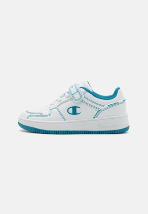 Witte lage sneaker met turquoise accenten, een klittenbandsluiting en een merklogo op de zijkant en hiel, gezien vanaf de buitenkant.