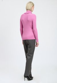 Enganliegende Langarm-Poloshirts mit geripptem, pinkfarbenem Stoff und einem gewellten Kragen, kombiniert mit grauen, maßgeschneiderten Hosen und schwarzen Pumps.