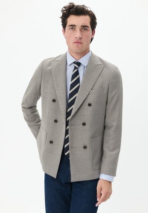 Double-breasted blazer in houndstooth pattern, light brown and cream, with dark buttons. Paired with a blue striped shirt and tie.