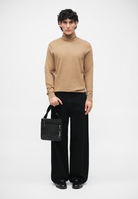Světlý rolák, černé kalhoty širokého střihu a malá černá taška s logem "Just Cavalli". Taška má zip a nastavitelný popruh.