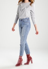 Maglietta grigia a maniche lunghe con scollatura arricciata, abbinata a jeans a vita alta azzurri chiari con leggere abrasioni. Stivaletti alla caviglia in velluto rosa.