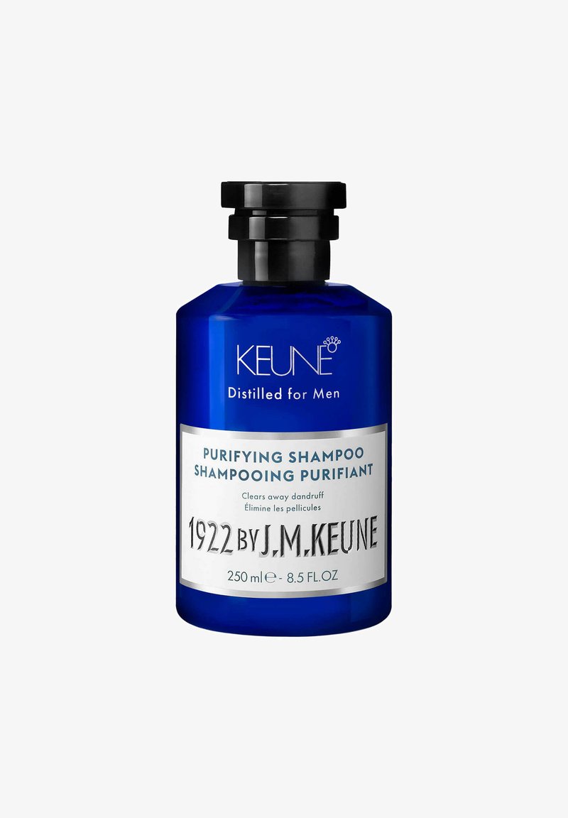Bouteille en verre bleu avec un bouchon à vis noir. L'étiquette présente un texte blanc détaillant le produit : "Shampoing Purifiant" et le nom de la marque "KEUNE." Taille de 250 ml.