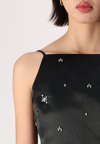 Black satin dress with thin straps, embellished with various rhinestones in different shapes on the bodice, creating a subtle decorative effect.