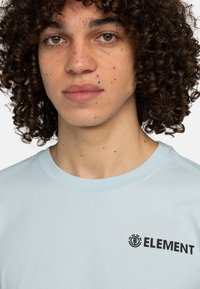 Light blue cotton t-shirt featuring a round neck, short sleeves, and a black "ELEMENT" logo on the left side. Smooth texture.