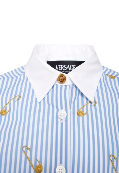 Chemise à rayures bleues et blanches avec des motifs de épingles de sécurité dorées et un col blanc. Présente une étiquette de logo et un accent de bouton doré.