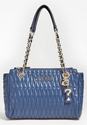 Blauwe doorgestikte leren Guess-handtas met gouden kettingriemen en een sleutelhanger met een vraagteken en ronde bedels.