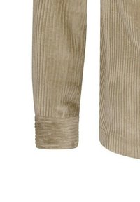 Haverkleurige corduroy mouw met verticale ribbels en een solide manchet. De textuur is zacht en benadrukt de rijke vezels van de stof en het gestructureerde ontwerp.