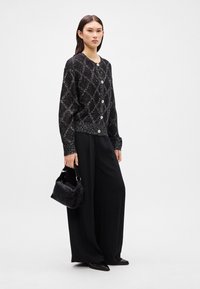 Black cardigan with silver speckles and diamond pattern, featuring round buttons. Paired with loose black pants and a small black handbag.