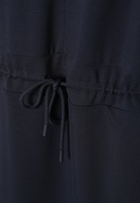 Navyblauwe jurk met een verzamelde taille, voorzien van een trekkoord. Zacht, glad materiaal met een subtiele textuur en zwarte aglets aan het trekkoord.