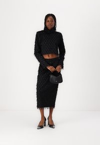 Black textured two-piece outfit with a cropped long-sleeve top and midi skirt, featuring a unique pattern and frayed edges. Paired with black heels and handbag.